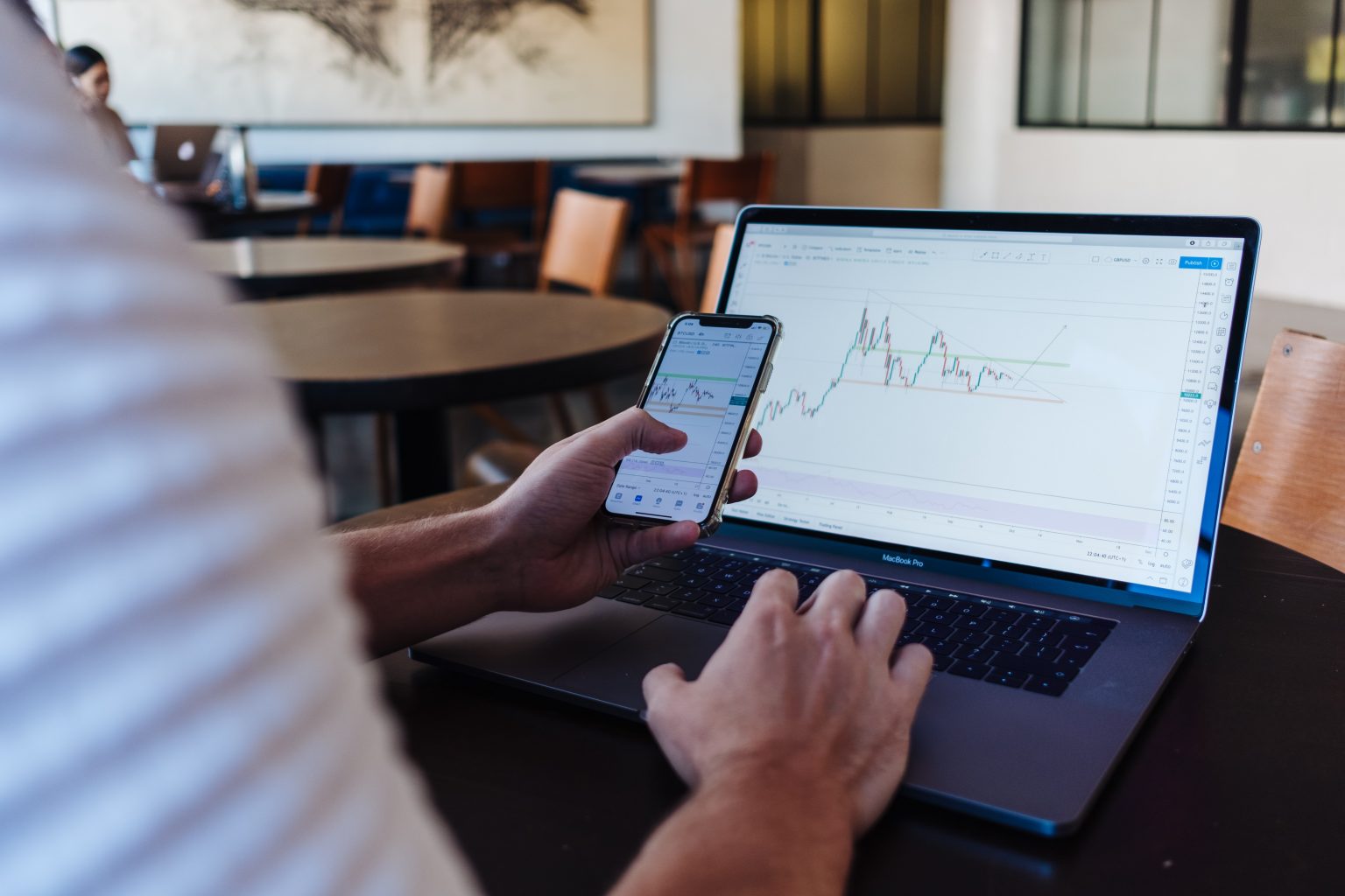 Mann sitzt vor einem Laptop. Mit seiner linken Hand schließt er einen Margin-Handel am Aktienmarkt ab. Mit der rechten Hand bedingt er den Laptop, dessen Screen einen Kurschart zeigt.